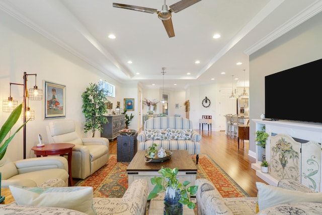 living room with light hardwood / wood-style floors, a raised ceiling, ornamental molding, and ceiling fan