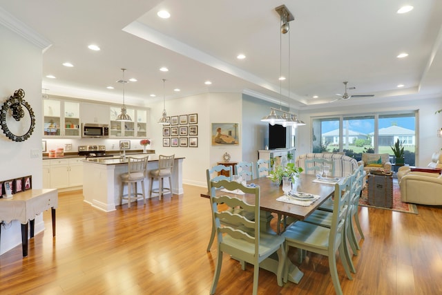 dining space featuring light hardwood / wood-style floors, sink, a tray ceiling, and ceiling fan