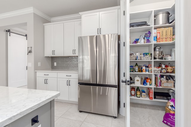 kitchen with crown molding, a barn door, white cabinetry, and stainless steel refrigerator