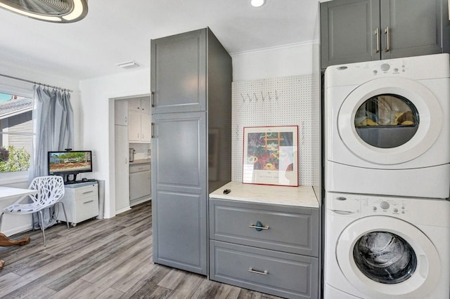 laundry room featuring ornamental molding, cabinet space, stacked washer and clothes dryer, and light wood-style floors