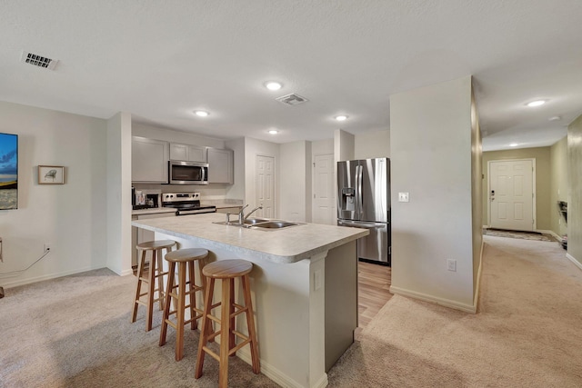 kitchen with light carpet, appliances with stainless steel finishes, sink, and a kitchen island with sink