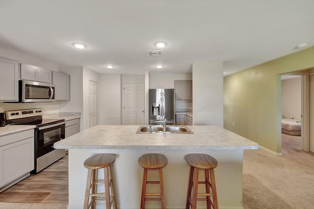 kitchen featuring light carpet, stainless steel appliances, a kitchen breakfast bar, and a kitchen island with sink