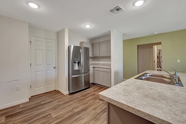 kitchen with light hardwood / wood-style flooring, stainless steel refrigerator with ice dispenser, sink, gray cabinets, and a textured ceiling