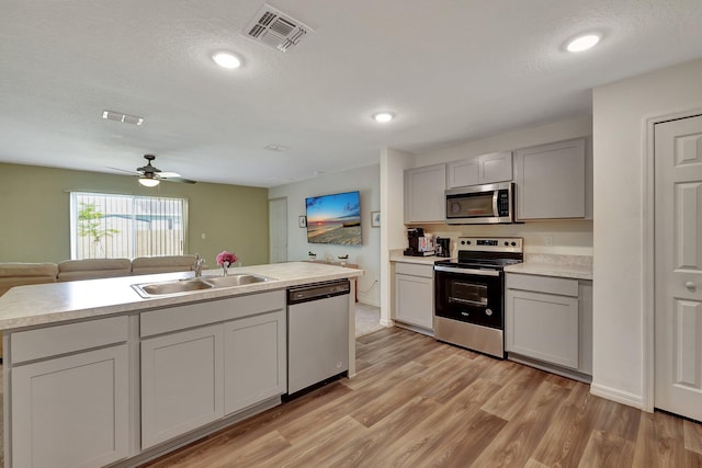 kitchen with an island with sink, appliances with stainless steel finishes, a textured ceiling, light hardwood / wood-style floors, and sink