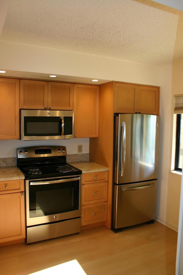 kitchen with stainless steel appliances, a textured ceiling, and light wood-type flooring