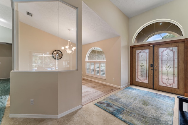 foyer with light wood-type flooring, french doors, a textured ceiling, a notable chandelier, and high vaulted ceiling