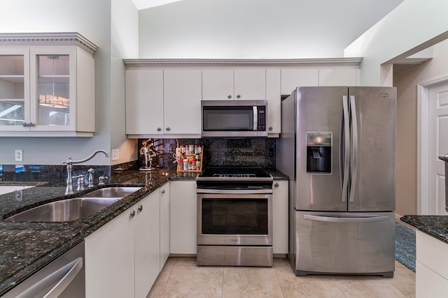 kitchen with dark stone counters, sink, vaulted ceiling, white cabinets, and appliances with stainless steel finishes