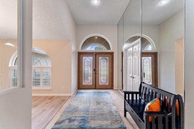 entryway featuring french doors, a textured ceiling, light hardwood / wood-style floors, and a high ceiling