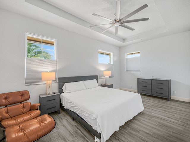 bedroom featuring ceiling fan, a raised ceiling, a textured ceiling, and light hardwood / wood-style floors