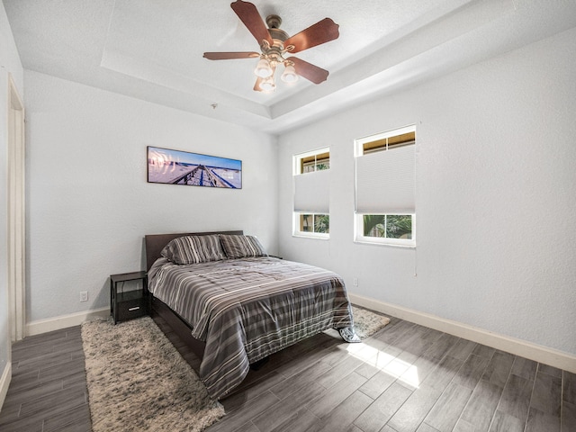 bedroom with ceiling fan, a raised ceiling, and dark hardwood / wood-style floors