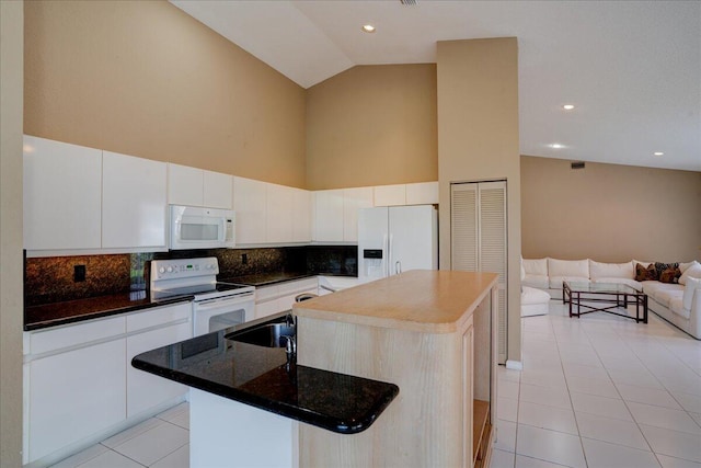 kitchen with decorative backsplash, white appliances, a kitchen island with sink, light tile patterned floors, and white cabinetry