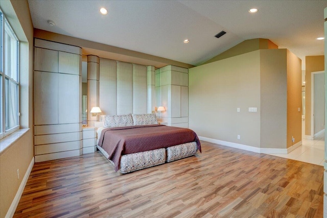 bedroom featuring light wood-type flooring, lofted ceiling, and a textured ceiling