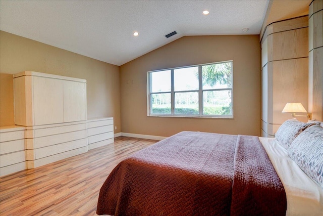 bedroom featuring a textured ceiling, light hardwood / wood-style floors, and lofted ceiling