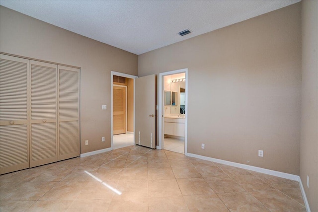 unfurnished bedroom with a textured ceiling, connected bathroom, a closet, and light tile patterned flooring