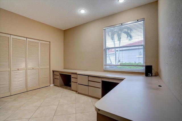 unfurnished office featuring built in desk, a textured ceiling, and light tile patterned floors