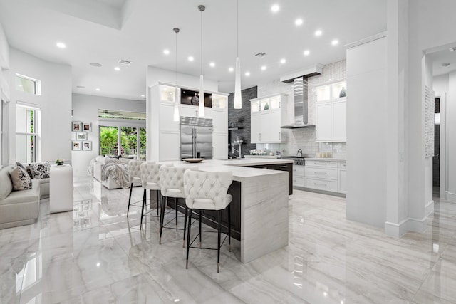 kitchen featuring wall chimney range hood, appliances with stainless steel finishes, a large island, pendant lighting, and white cabinets