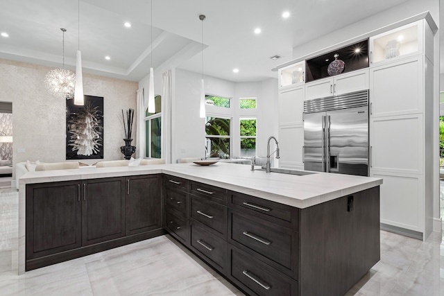 kitchen featuring stainless steel built in fridge, white cabinets, hanging light fixtures, and a kitchen island with sink