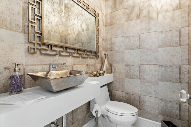 bathroom with toilet, sink, and tile walls