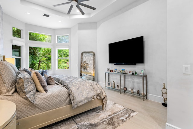 bedroom with a high ceiling, a raised ceiling, light hardwood / wood-style floors, and ceiling fan