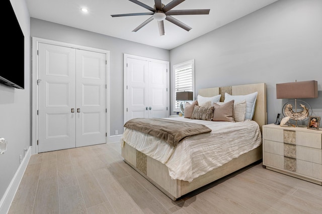 bedroom with light hardwood / wood-style flooring, multiple closets, and ceiling fan