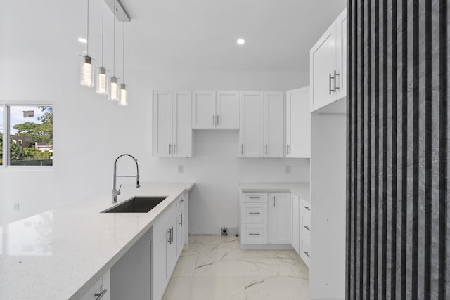 kitchen featuring pendant lighting, sink, light stone countertops, and white cabinets