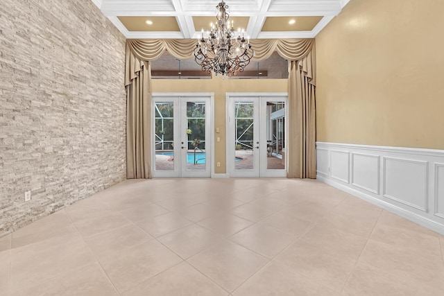 spare room featuring an inviting chandelier, french doors, coffered ceiling, and crown molding