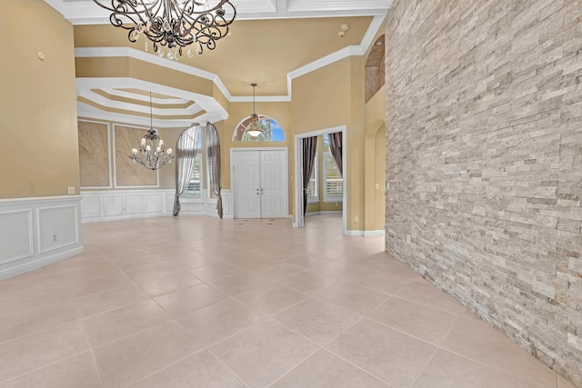 entrance foyer with ornamental molding, a high ceiling, an inviting chandelier, and light tile patterned floors