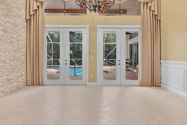 doorway to outside with french doors, light tile patterned flooring, an inviting chandelier, and a high ceiling