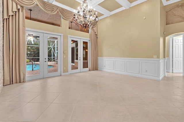 unfurnished room featuring french doors, a towering ceiling, light tile patterned floors, and a chandelier