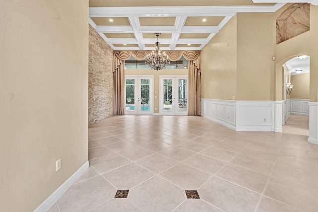 tiled empty room featuring an inviting chandelier, crown molding, beamed ceiling, french doors, and coffered ceiling