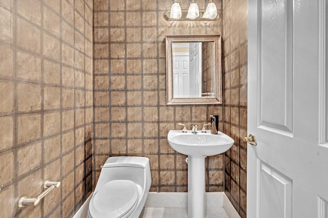 bathroom featuring toilet, tile patterned floors, tile walls, and sink