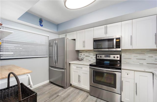 kitchen with backsplash, white cabinetry, light stone countertops, light wood-type flooring, and stainless steel appliances