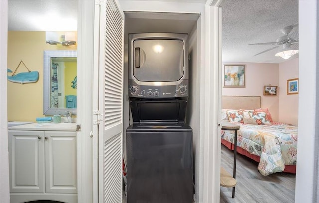 laundry area featuring stacked washer and dryer, sink, a textured ceiling, light hardwood / wood-style floors, and ceiling fan