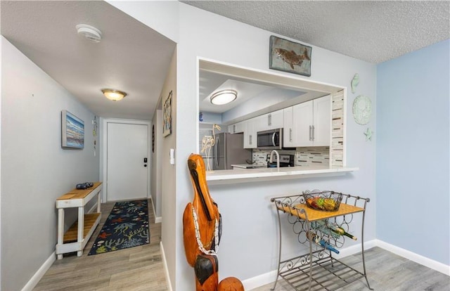 kitchen with stainless steel appliances, backsplash, white cabinetry, a textured ceiling, and light hardwood / wood-style floors