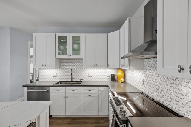 kitchen with a sink, stainless steel appliances, wall chimney range hood, white cabinetry, and backsplash