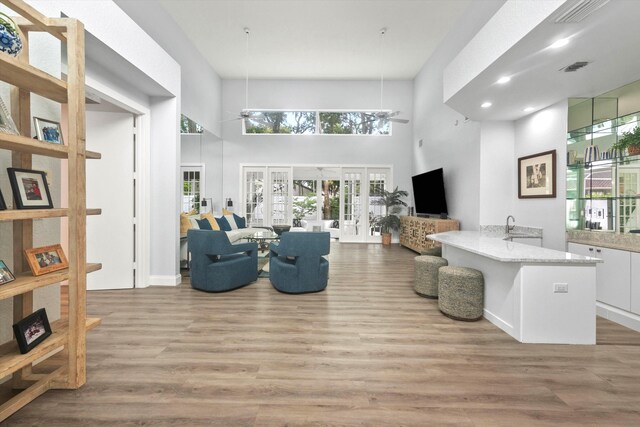 living room featuring ceiling fan, wood finished floors, a towering ceiling, visible vents, and french doors