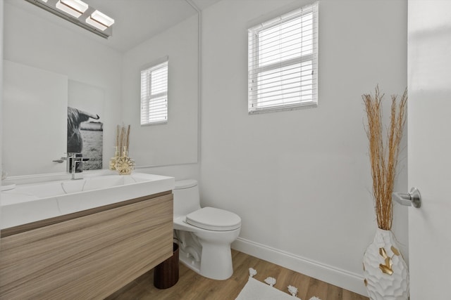 half bath with toilet, baseboards, wood finished floors, and vanity