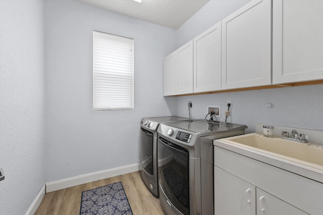 laundry room featuring separate washer and dryer, light wood-type flooring, cabinet space, and baseboards