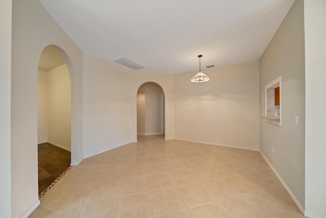 spare room featuring arched walkways, baseboards, and light tile patterned floors