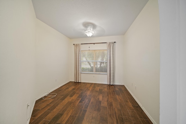 spare room featuring a textured ceiling, dark wood-type flooring, and baseboards