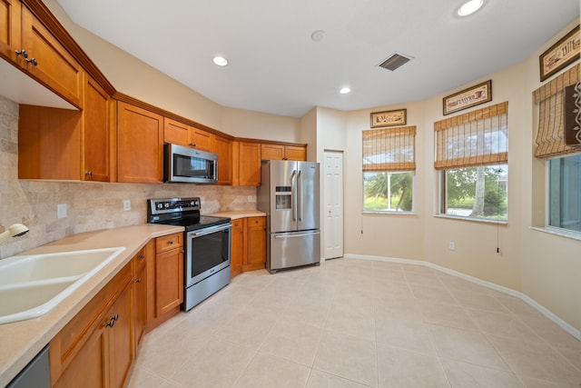 kitchen with appliances with stainless steel finishes, brown cabinetry, light countertops, and a sink