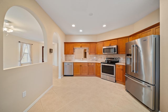 kitchen with stainless steel appliances, light countertops, backsplash, a sink, and baseboards