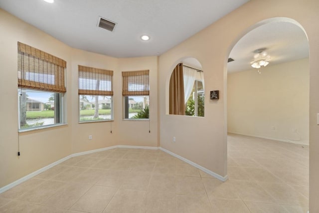 spare room featuring light tile patterned floors, arched walkways, recessed lighting, visible vents, and baseboards