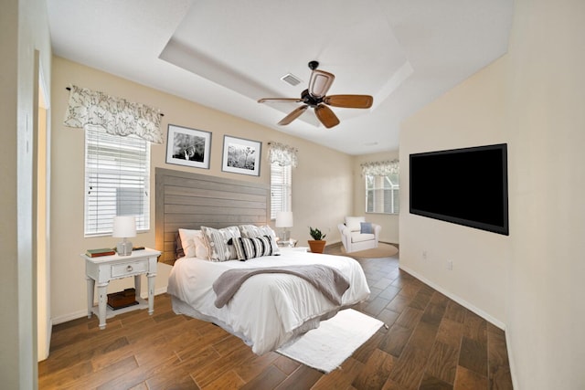 bedroom with a tray ceiling, multiple windows, and dark wood finished floors