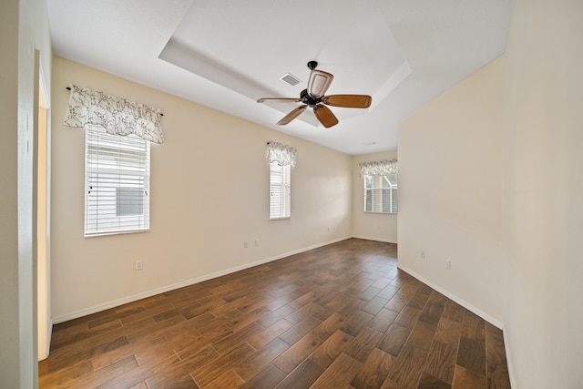 empty room featuring dark wood-style floors, a raised ceiling, visible vents, a ceiling fan, and baseboards