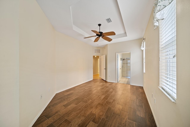 interior space featuring dark wood-type flooring, a raised ceiling, visible vents, and baseboards