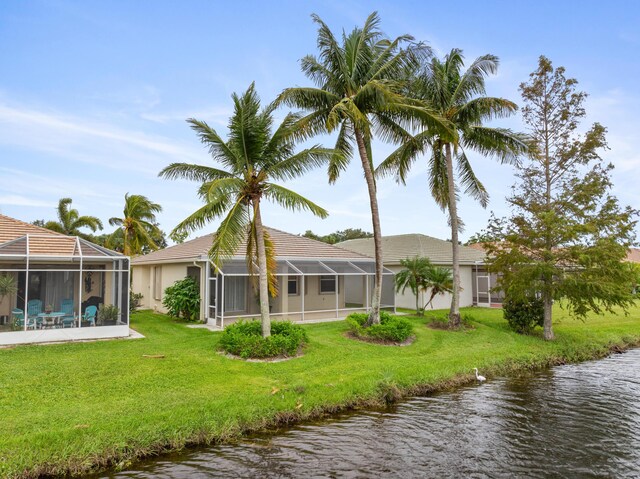 rear view of property with glass enclosure, a yard, and a water view