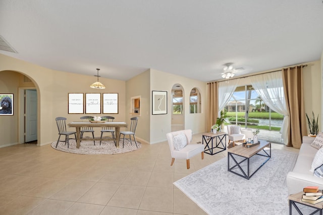 living area featuring light tile patterned floors, visible vents, arched walkways, and baseboards