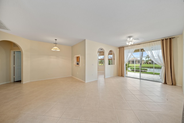 empty room featuring arched walkways, visible vents, baseboards, and light tile patterned floors