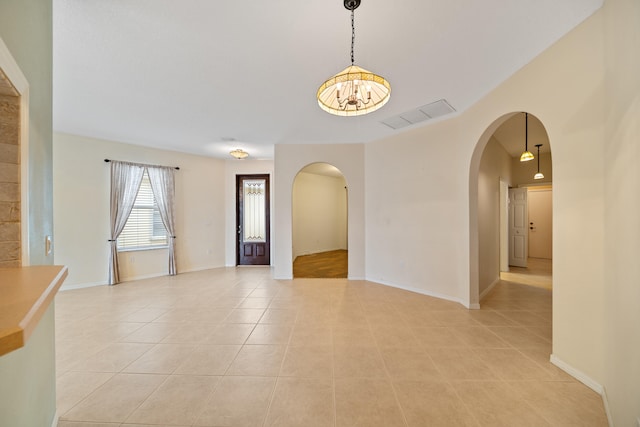 empty room featuring baseboards, visible vents, arched walkways, and light tile patterned flooring